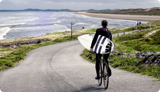 A person carrying a surfboard while riding on a bicycle