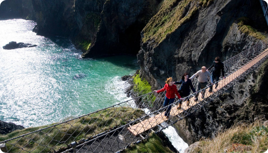 A group of people walking on a rope bridge over a cliff